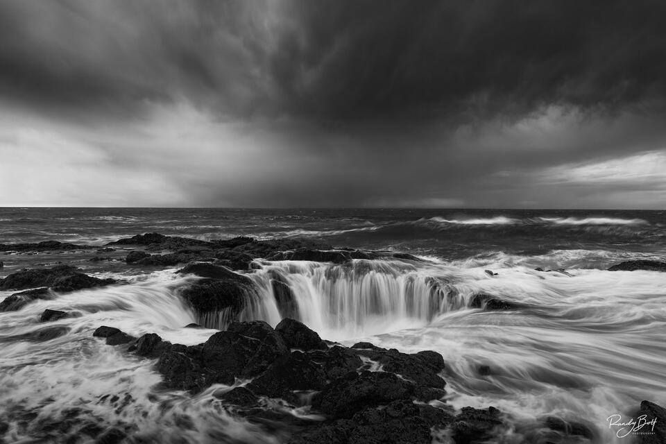 Thor's Well in Cape Perpetua during sunset with a storm in the background as a black and white image